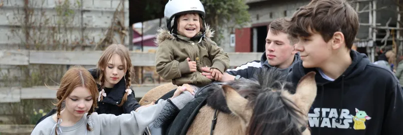 Three-year-old Vasylisa* sits calmly with assistance from volunteers during therapeutic horse riding for children who are displaced and affected by war.MCC, with partner Association of Mennonite B